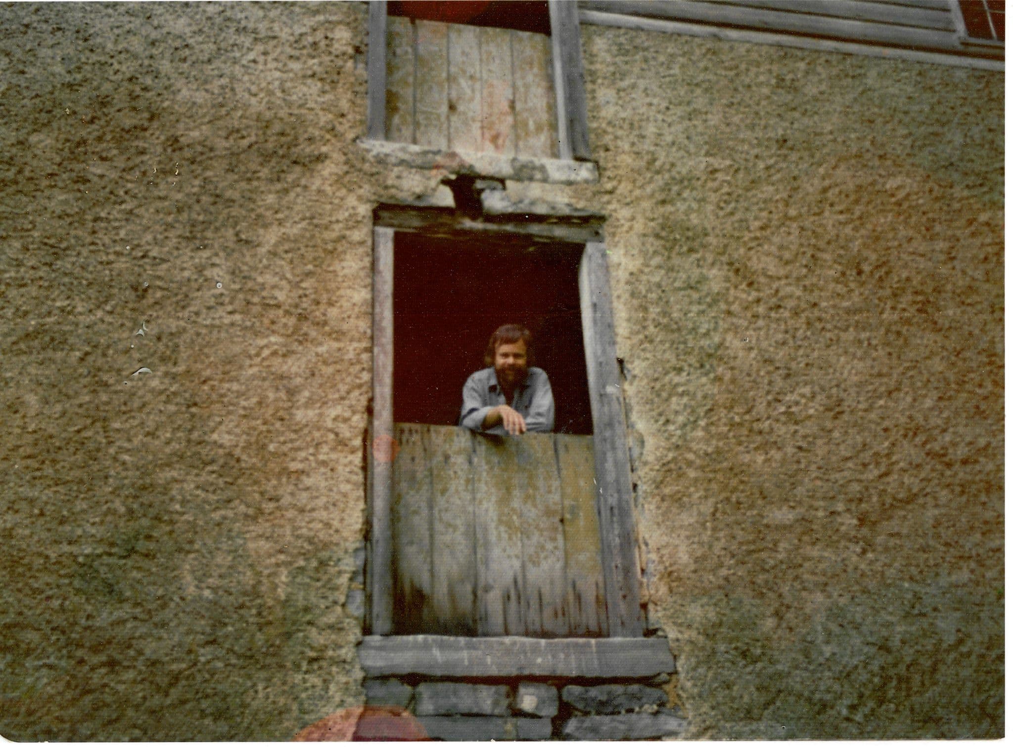 Charles Buckley leaning out of the mill's upper loading door, arms resting on the weathered boards