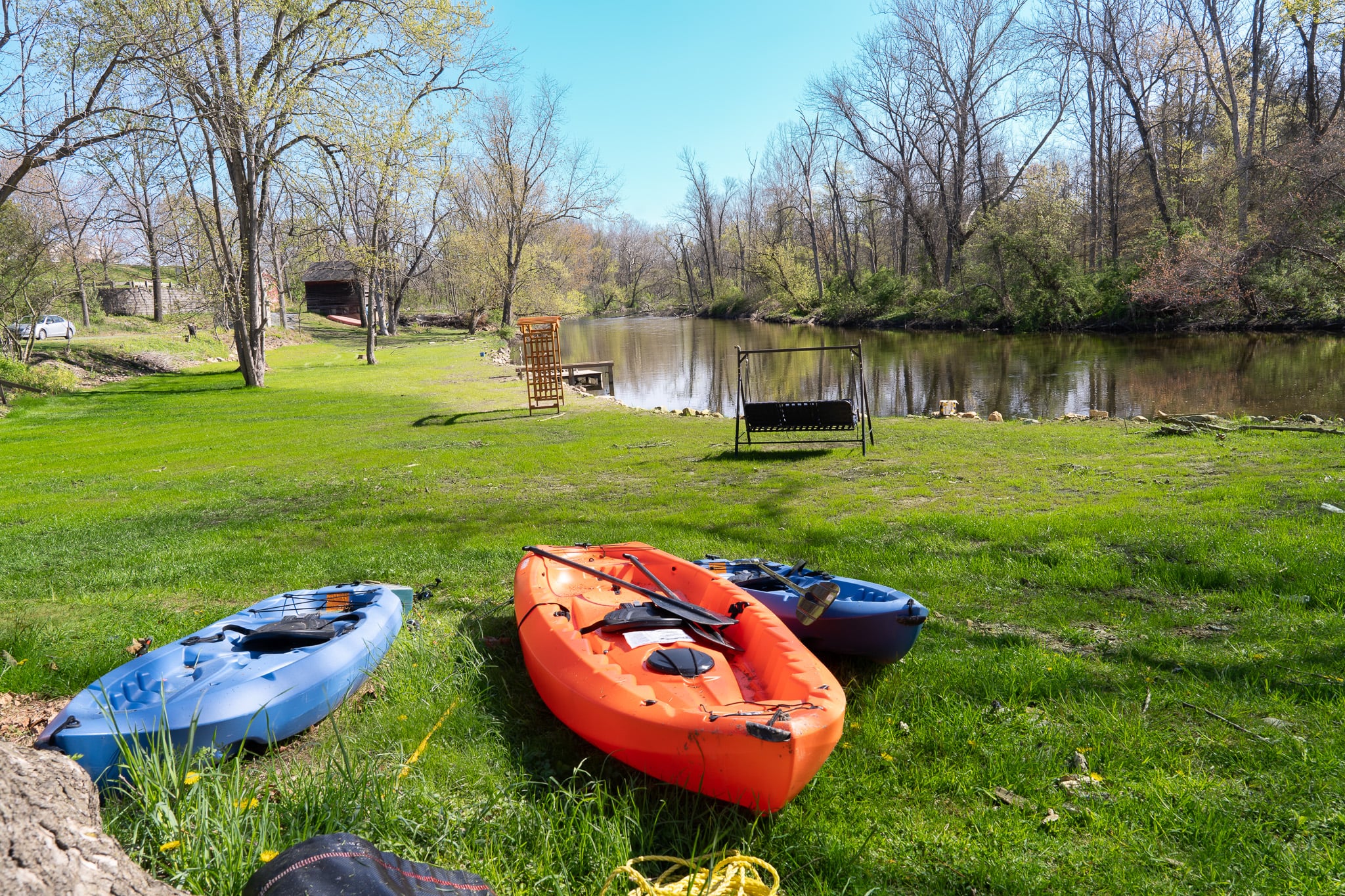 Kayaks on the lawn beside the Musconetcong River with rocking chair